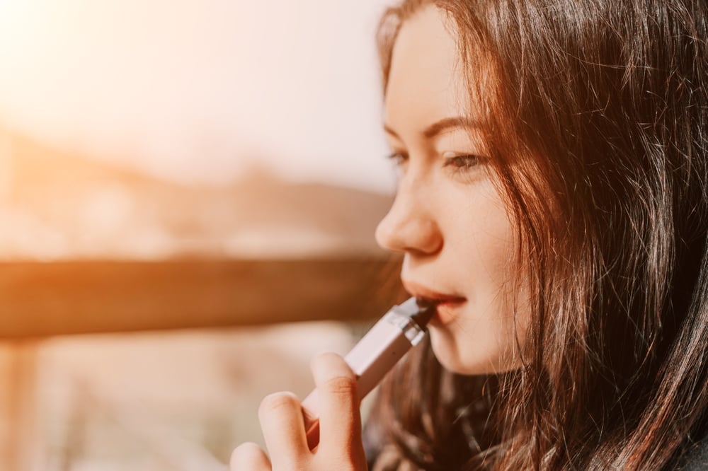Tânără care inhalează dintr-un POD vape cu auto-draw, în aer liber
