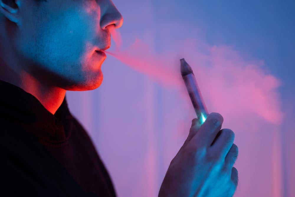 Bărbat adult care folosește o țigară electronică de tip pen, în lumină albastră și roșie